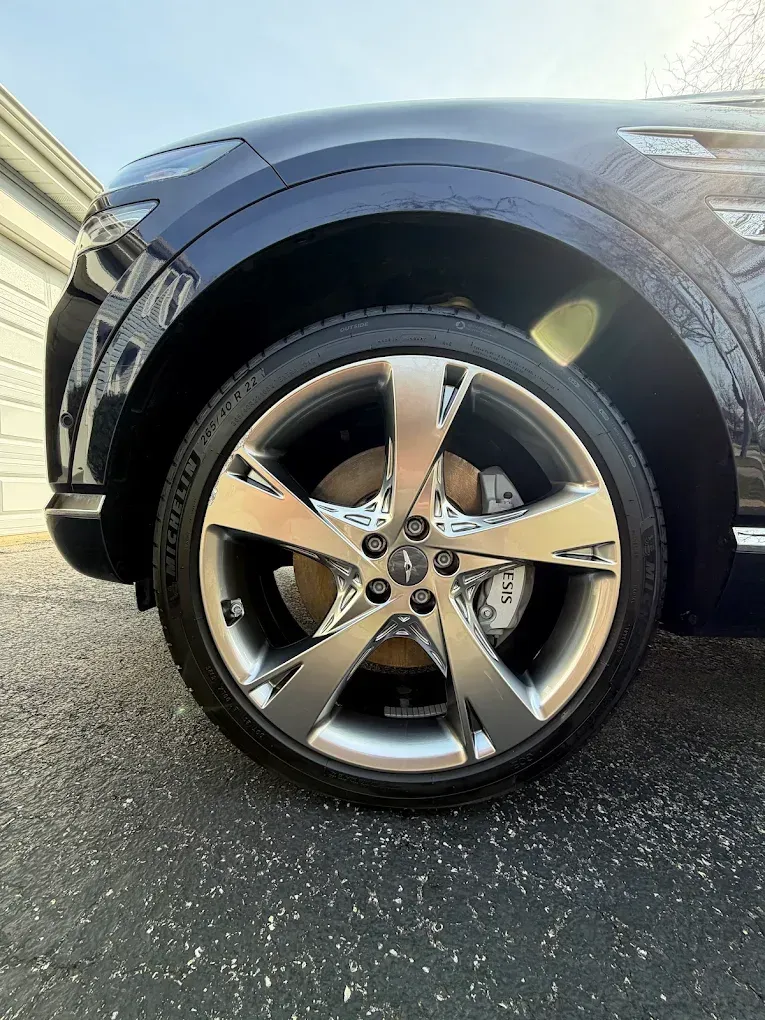 Close-up of a black SUV’s front wheel with chrome five-spoke rim on a driveway.