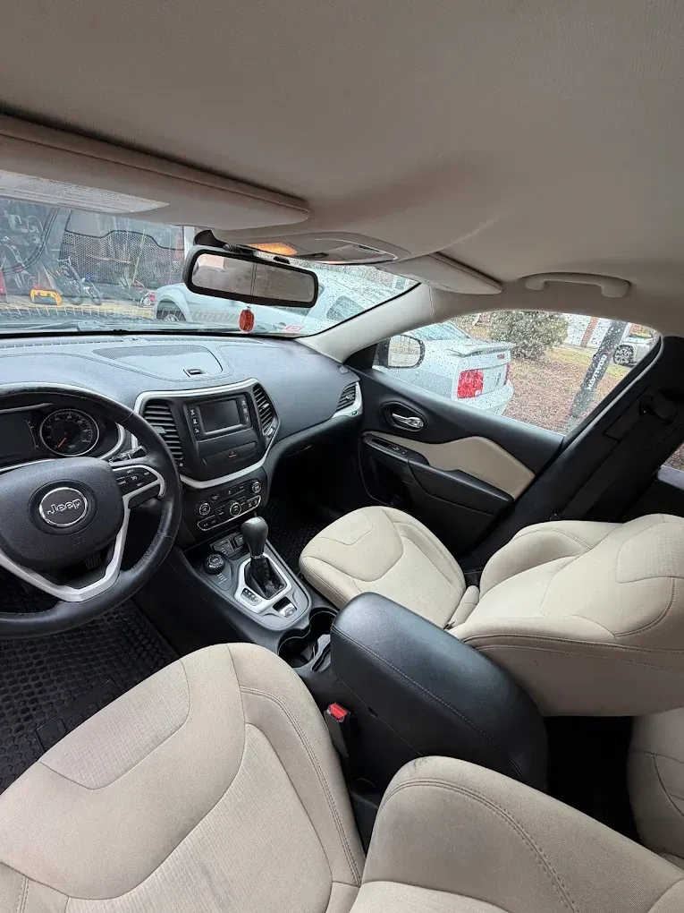 Car interior with beige seats, black dashboard, and rearview mirror on a rainy day