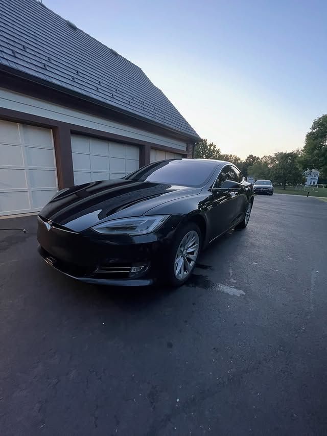 Black Tesla parked beside a garage at dusk