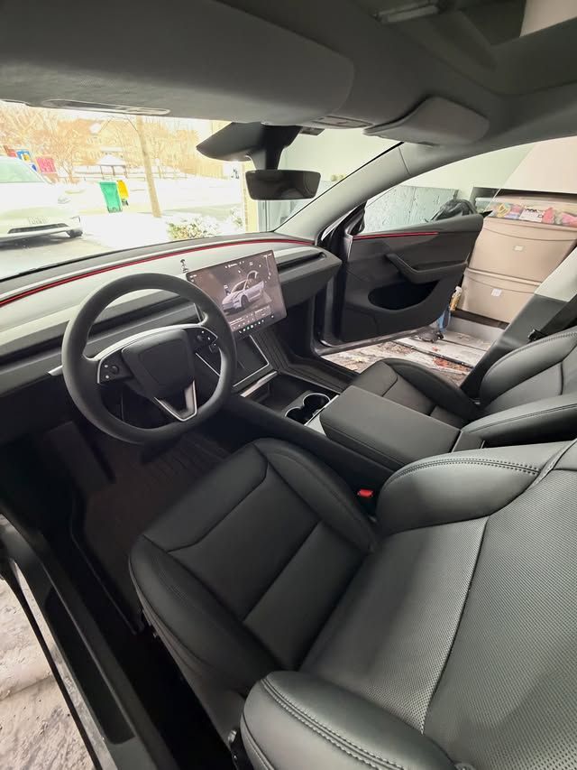 Modern car interior with black seats, dashboard display, and steering wheel, viewed from the driver’s side