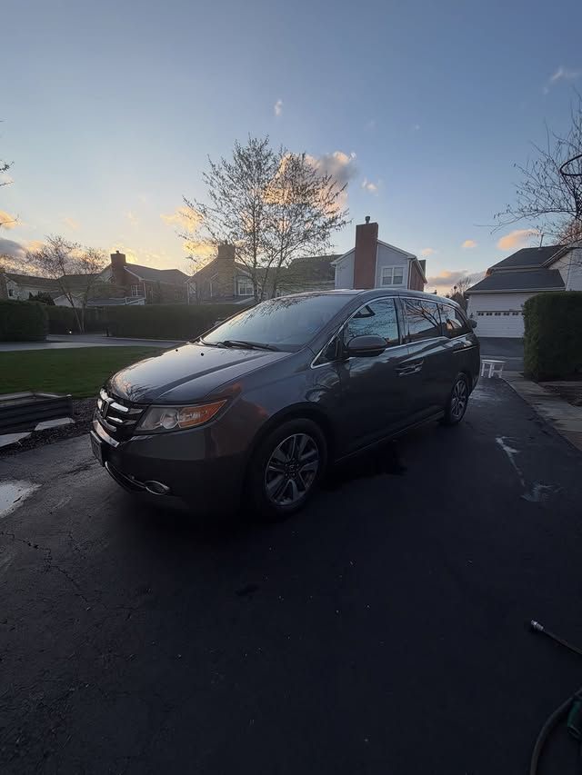 Dark gray minivan parked in a driveway at sunset, with houses and a tree in the background