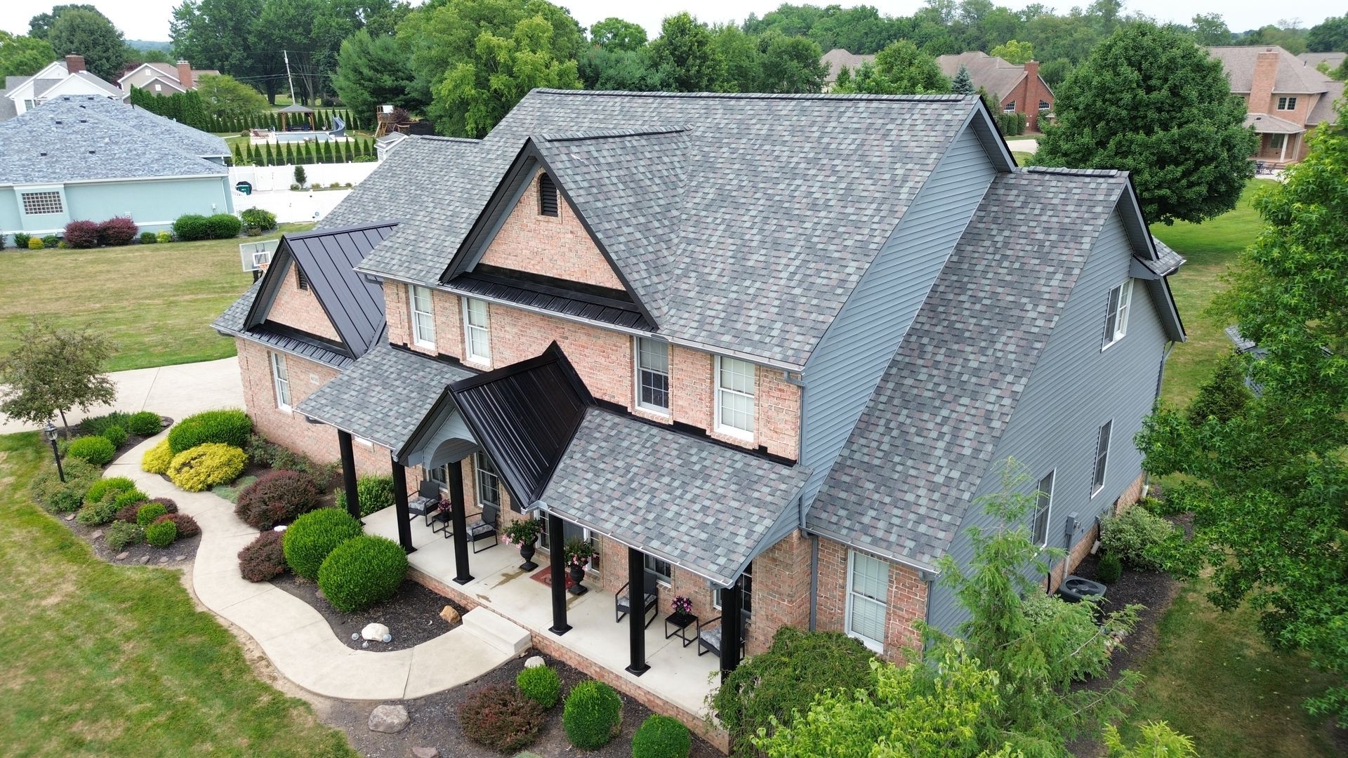 An aerial view of a large brick house with a gray roof surrounded by trees.