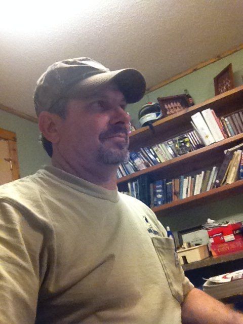 a man wearing a hat is standing in front of a bookshelf