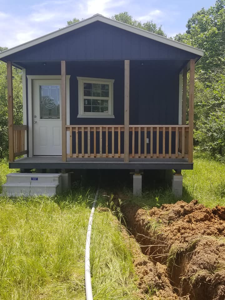 a small house with a porch is sitting in the middle of a grassy field .