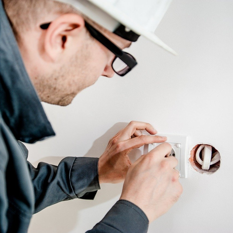 a man wearing a hard hat and glasses is working on an electrical outlet