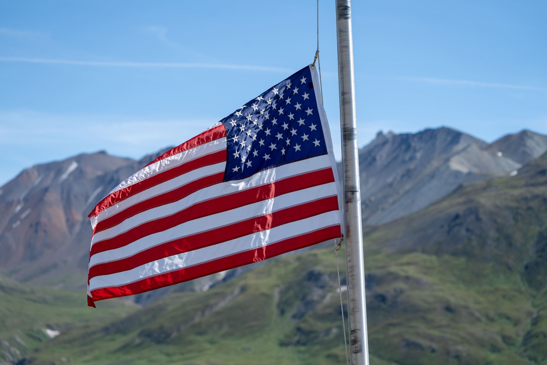 An american flag is waving in the wind in front of a mountain.