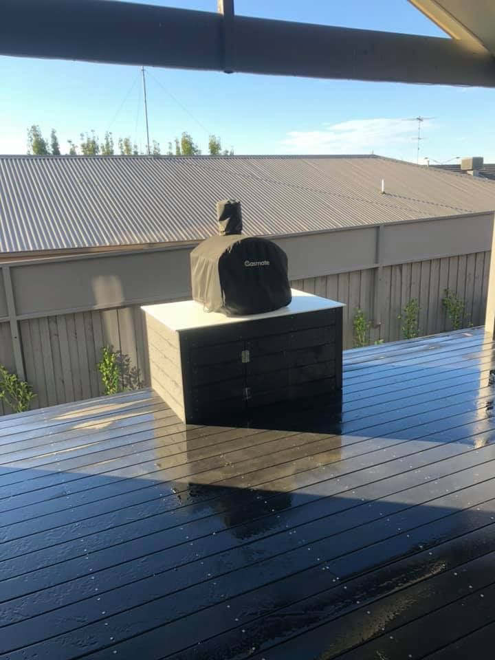 A black pizza oven on a wooden deck, set against a backdrop of a fence and roof — MGP Landscaping in Geelong, VIC 