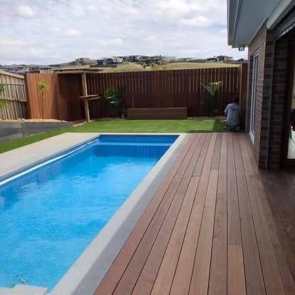 Pool with wooden deck and lawn in a backyard, brown fence, person working near the house — MGP Landscaping in Geelong, VIC