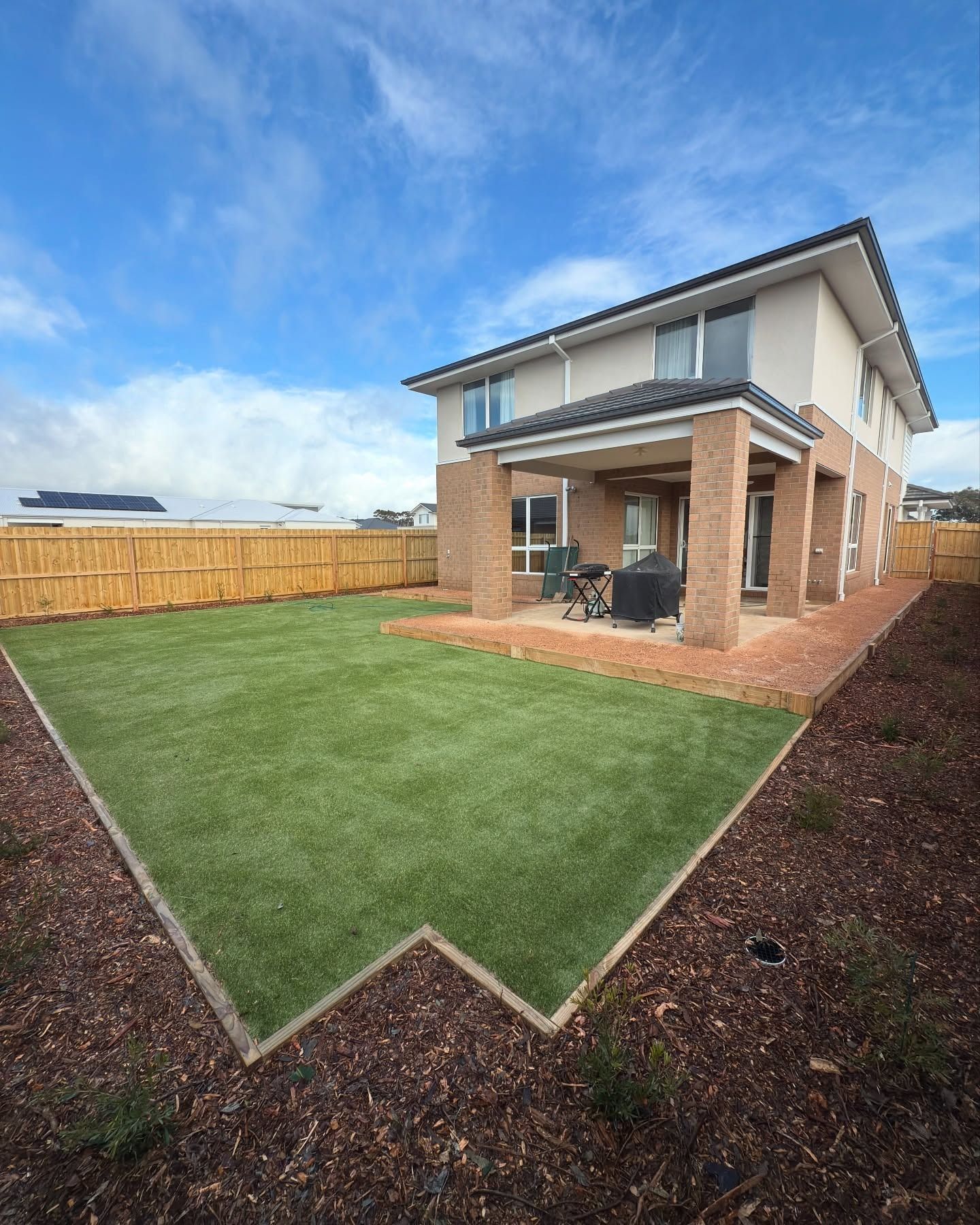 Backyard with green lawn, brick columns, and a two-story beige house — MGP Landscaping in Geelong, VIC 