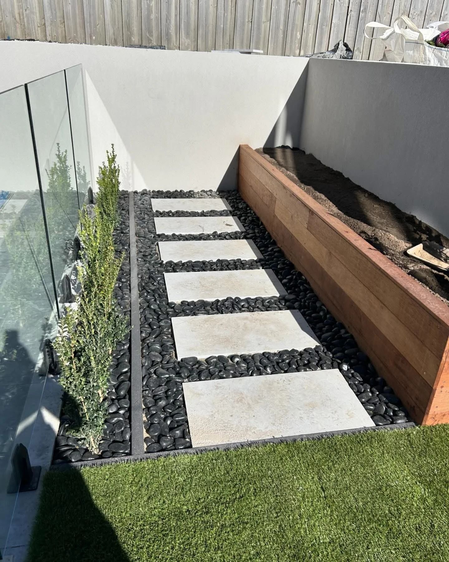 Pathway of stone pavers and black rocks bordered by greenery and a wood planter — MGP Landscaping in Geelong, VIC 