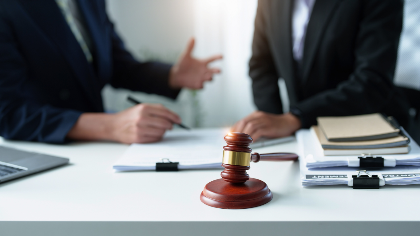 Judge's gavel on a desk during a legal meeting with two people in suits discussing documents