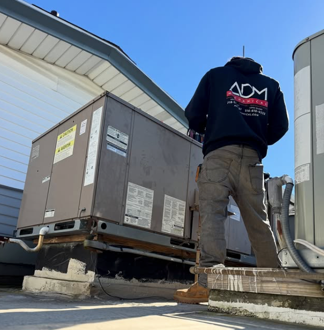 A man is installing an air conditioner on the side of a house.