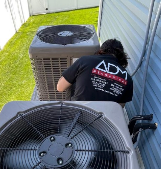 A gray air conditioner is sitting on a concrete platform outside of a house.