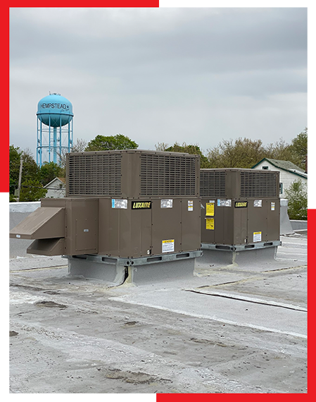 Two air conditioners are sitting on top of a roof with a water tower in the background.