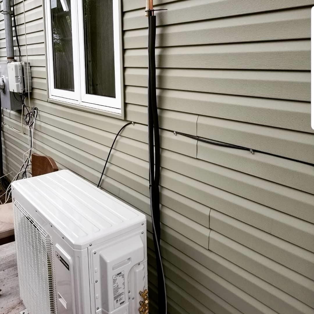 A white air conditioner is sitting on the side of a house next to a window.