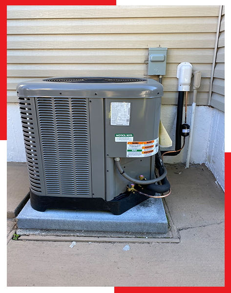 A gray air conditioner is sitting on a concrete platform outside of a house.