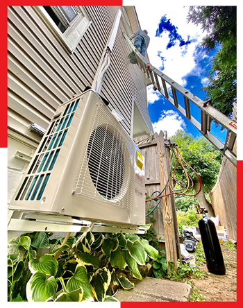 A man is installing an air conditioner on the side of a house.