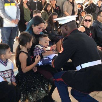 US military member presenting folded American Flag to military family at funeral