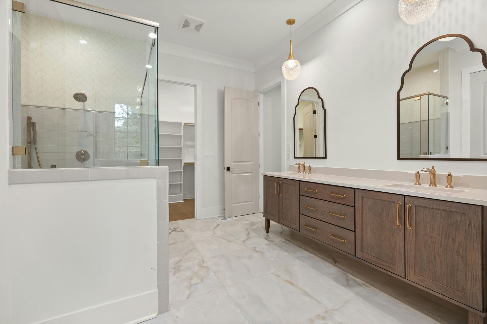 Modern bathroom with glass shower, double vanity, and marble-style tile floor