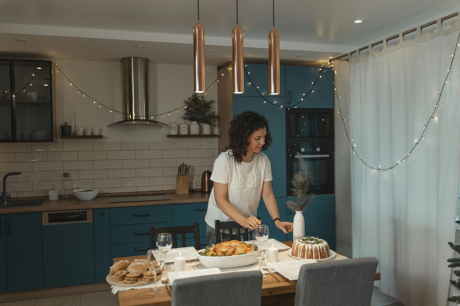 Woman setting a table in a decorated kitchen; roast chicken, cake, and beautiful kitchen cabinets.