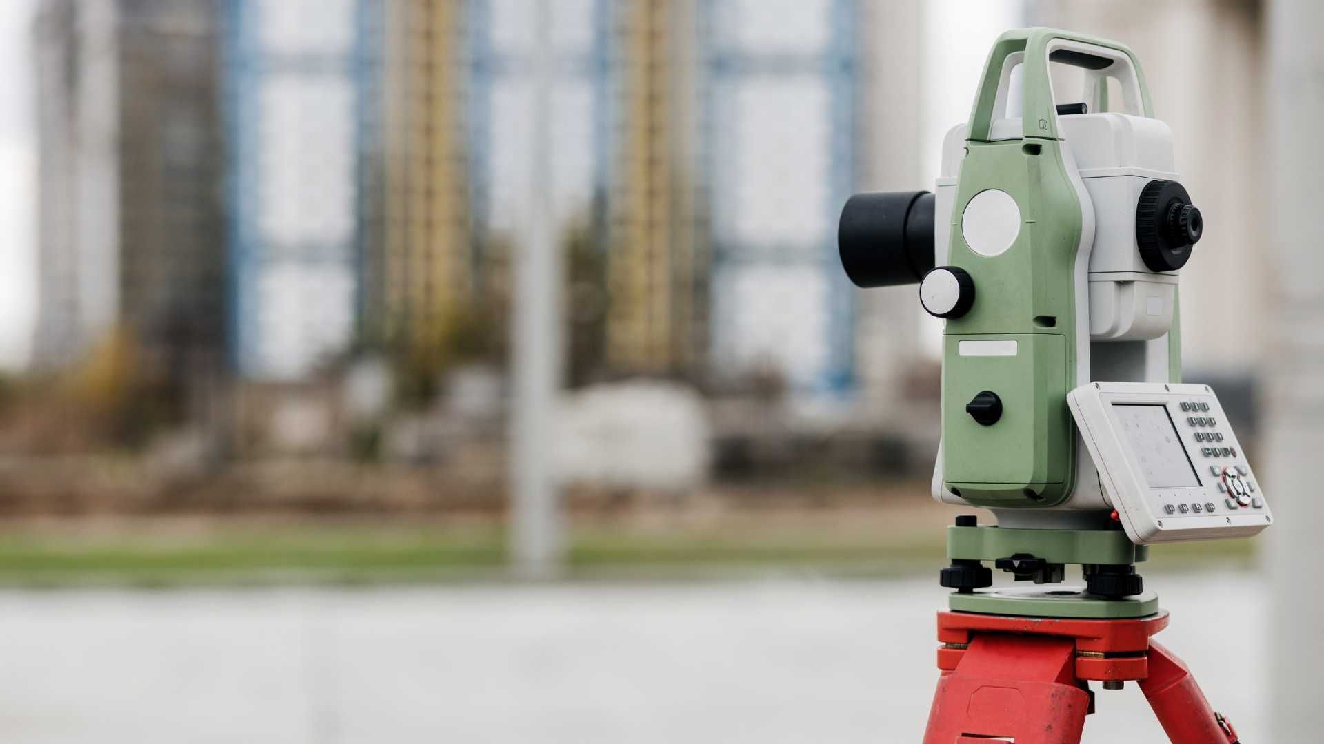 A theodolite is sitting on a tripod in front of a building.