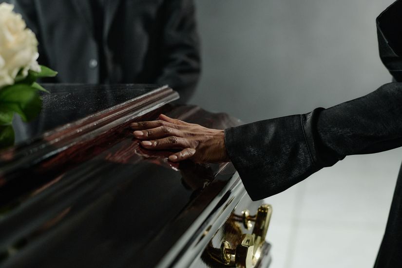 Person in black coat places red rose on a tombstone in a sunlit cemetery. Person in black coat places red rose on a tombstone in a sunlit cemetery.
