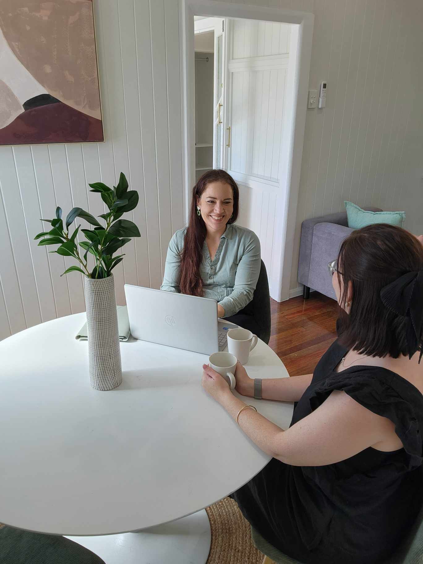 Two Women Are Sitting At A Table With A Laptop — Emmel Finance in Townsville, QLD
