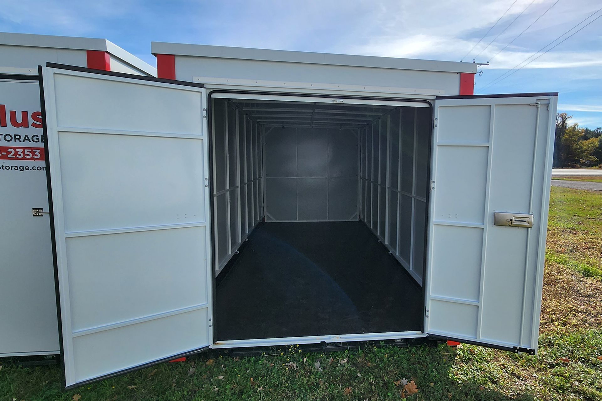 A white storage container with the doors open is sitting in the grass.