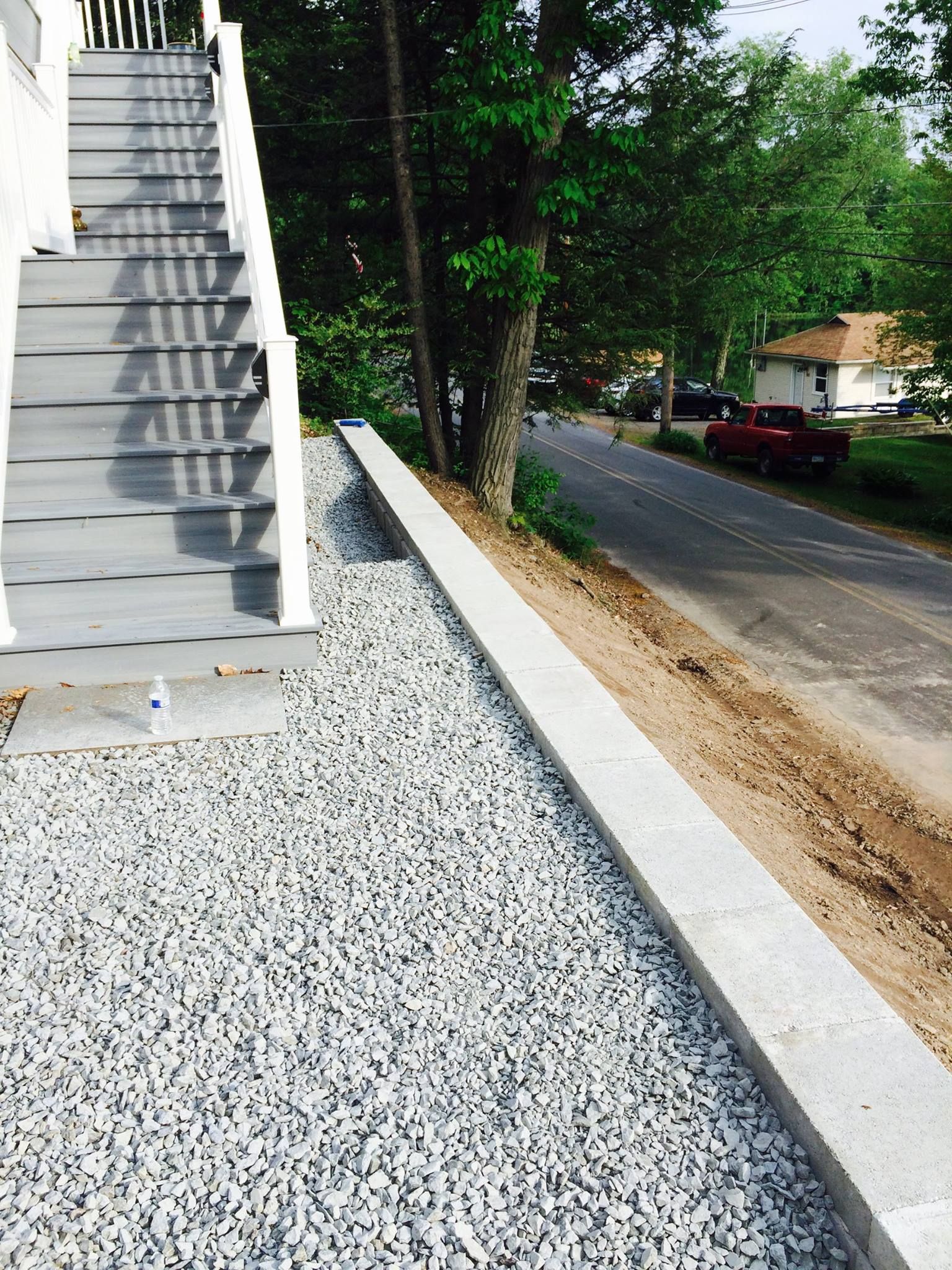 Gray stairs next to a gravel area, a concrete retaining wall, and a road.