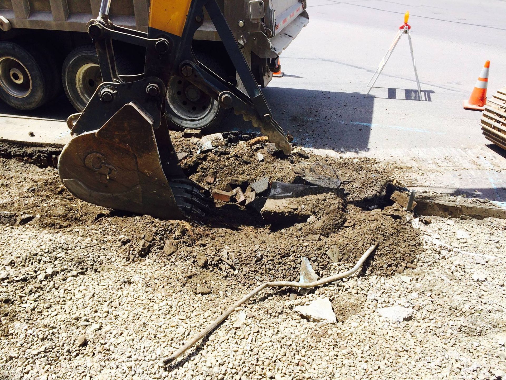 Excavator bucket digging into the ground on a street, part of road construction.