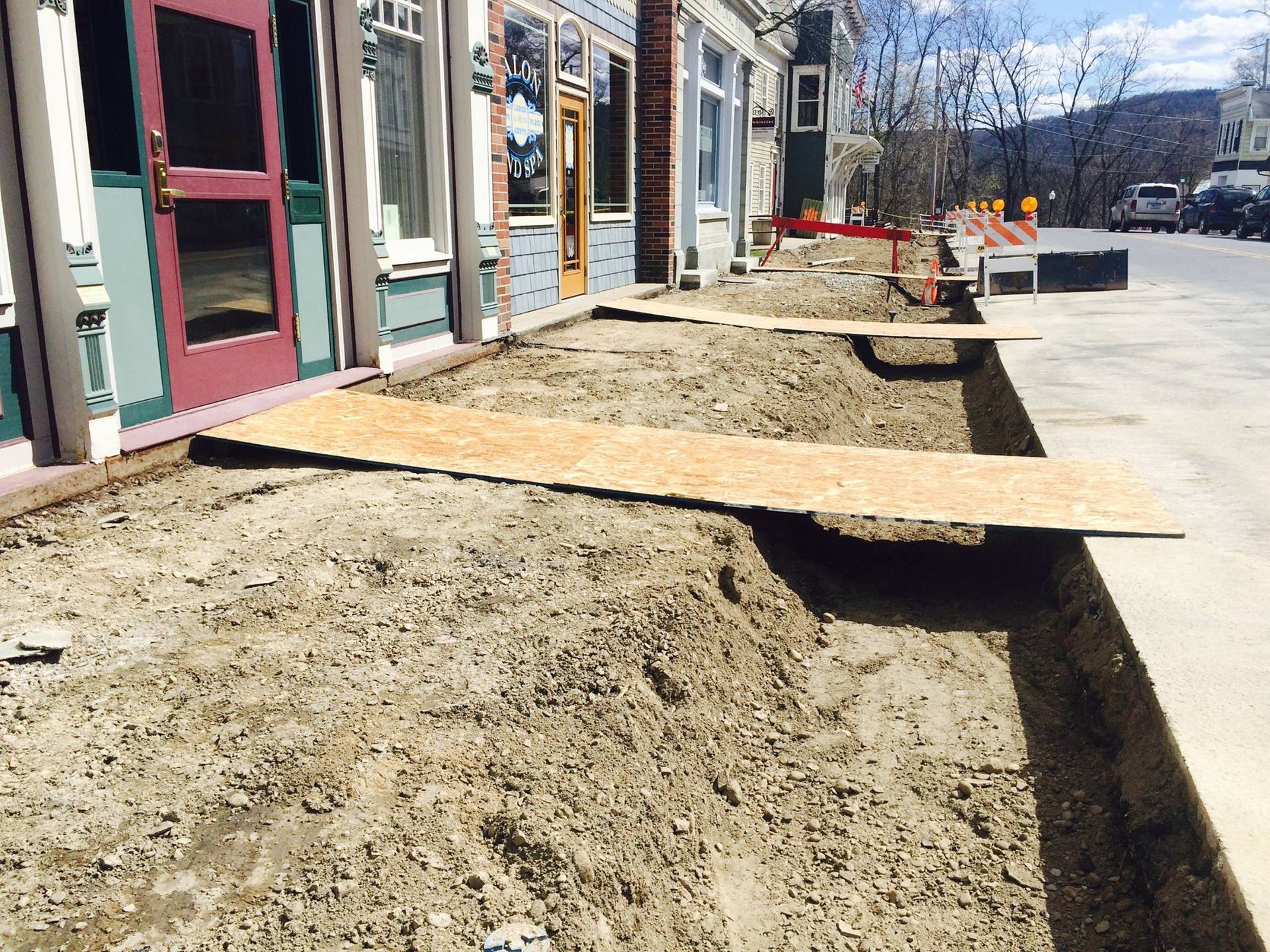 Sidewalk construction with planks laid over trenches in front of storefronts.