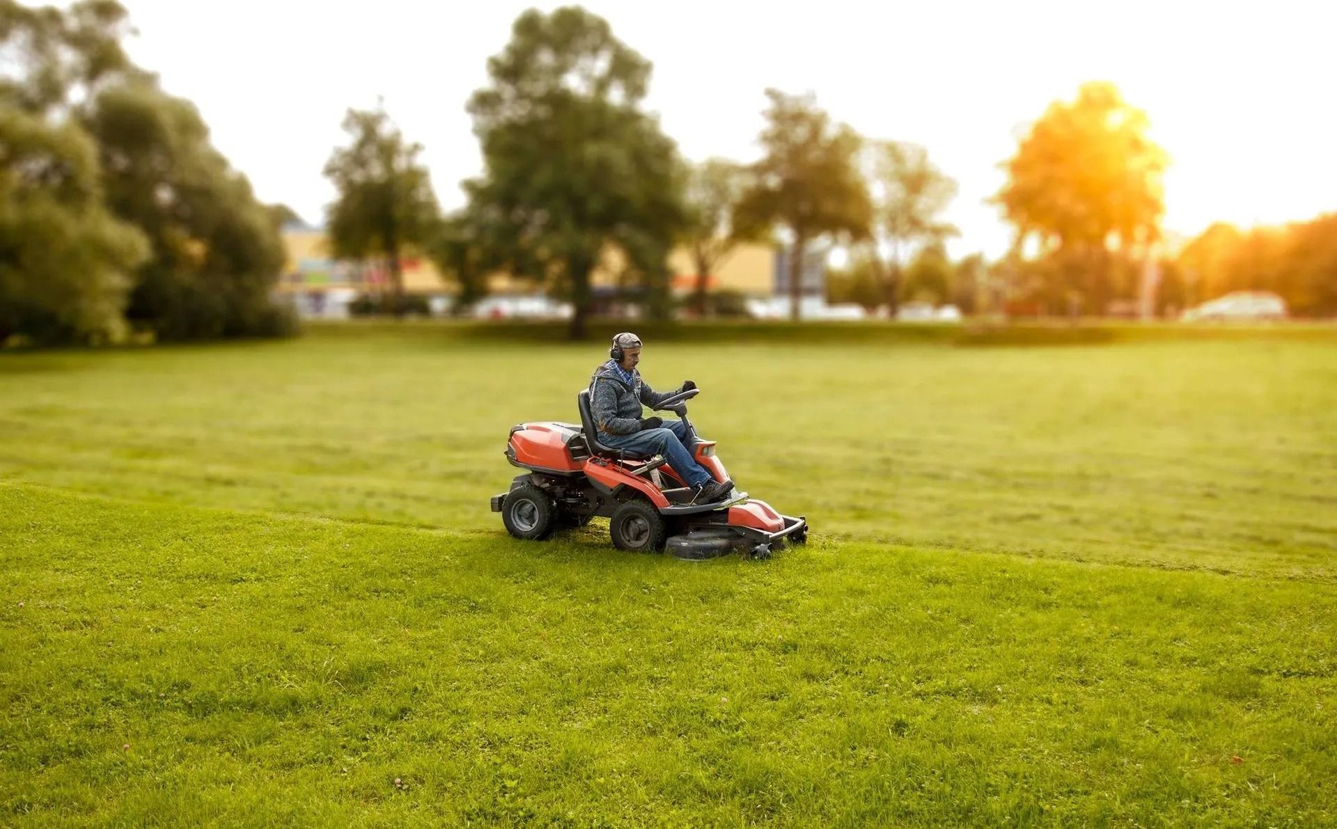 Man on riding lawn mower cutting grass in a sunny park.