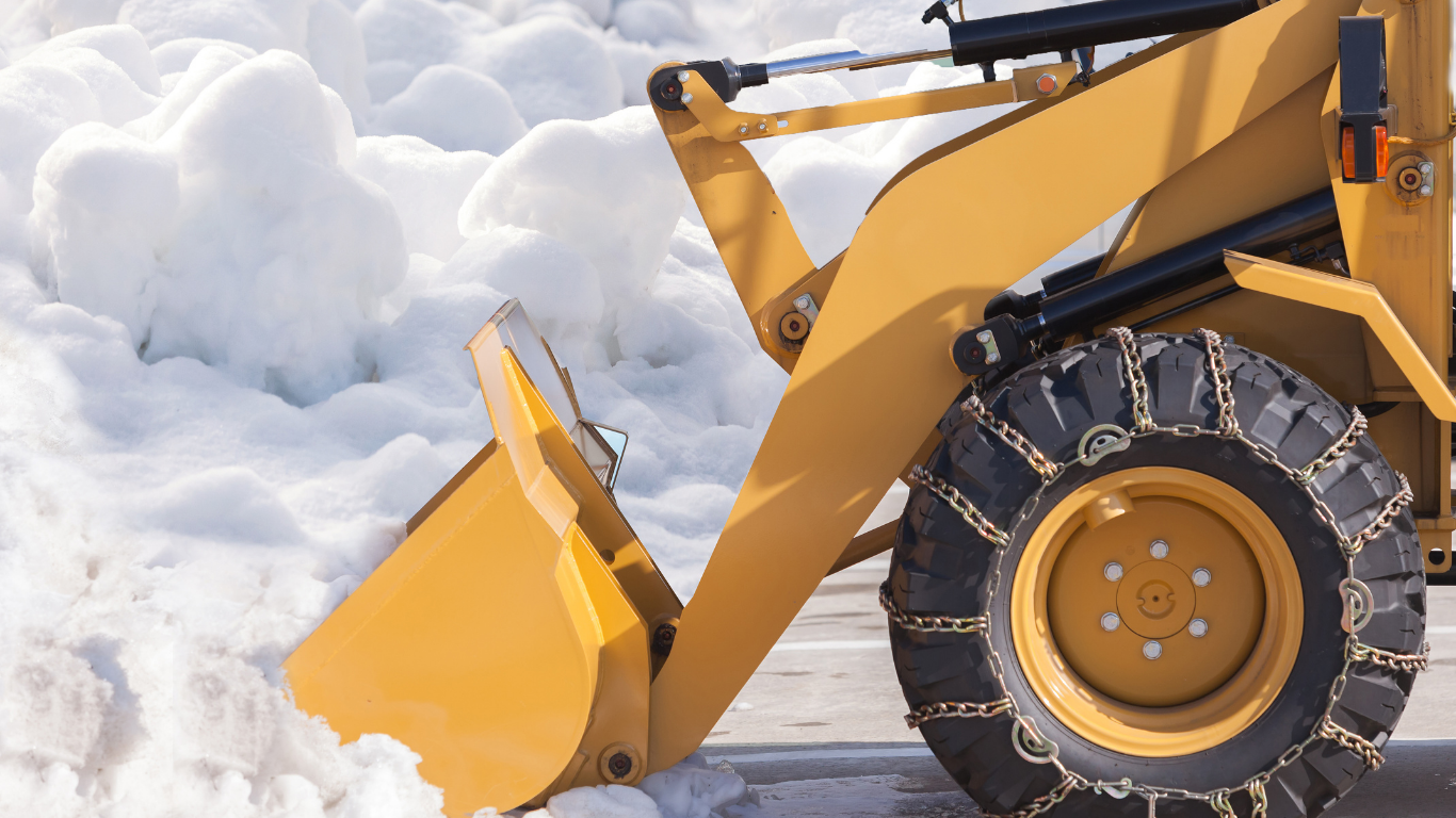 Yellow snowplow with chains on tire removing snow.