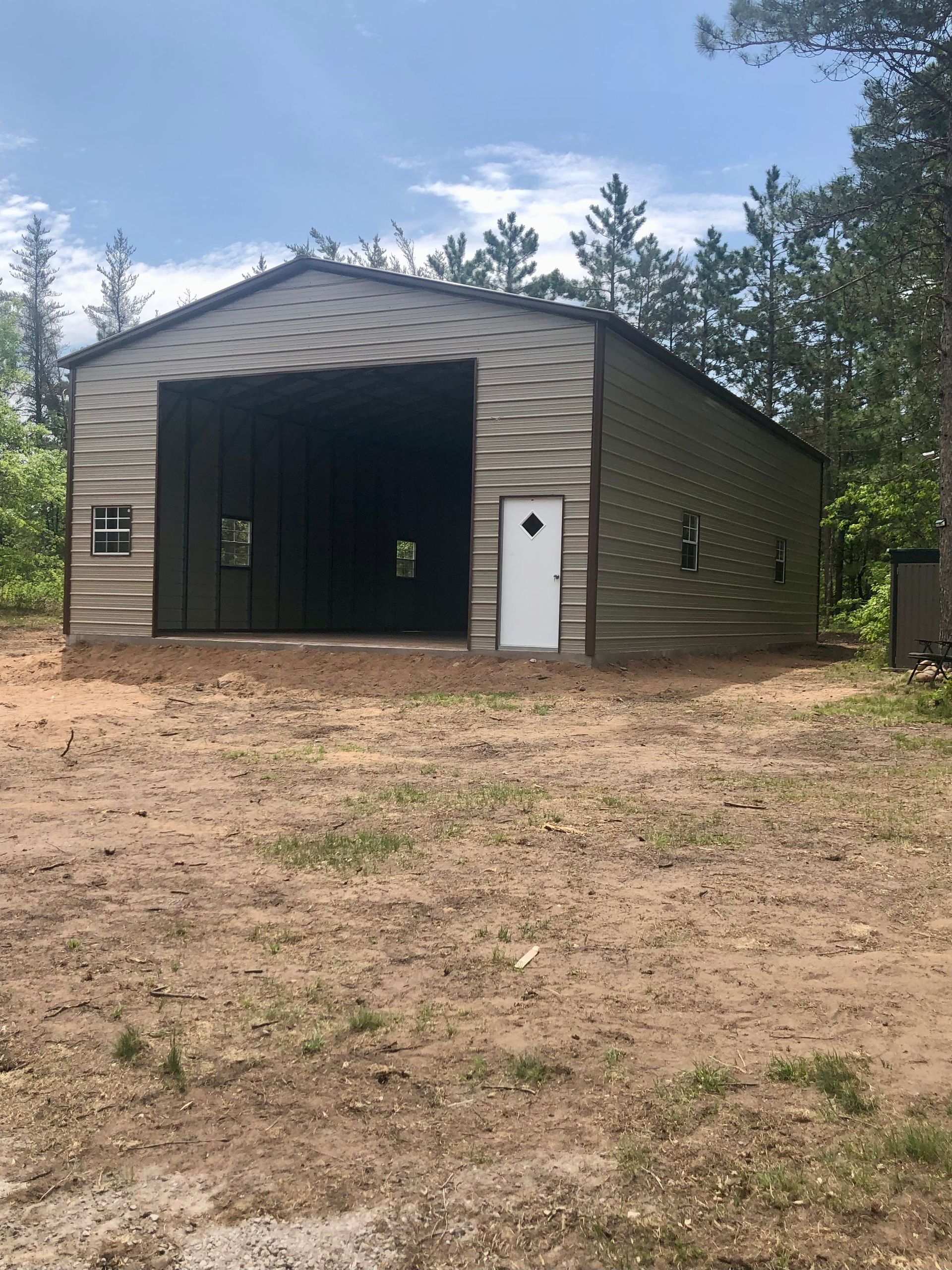 A large metal building with a white door is sitting in the middle of a dirt field.