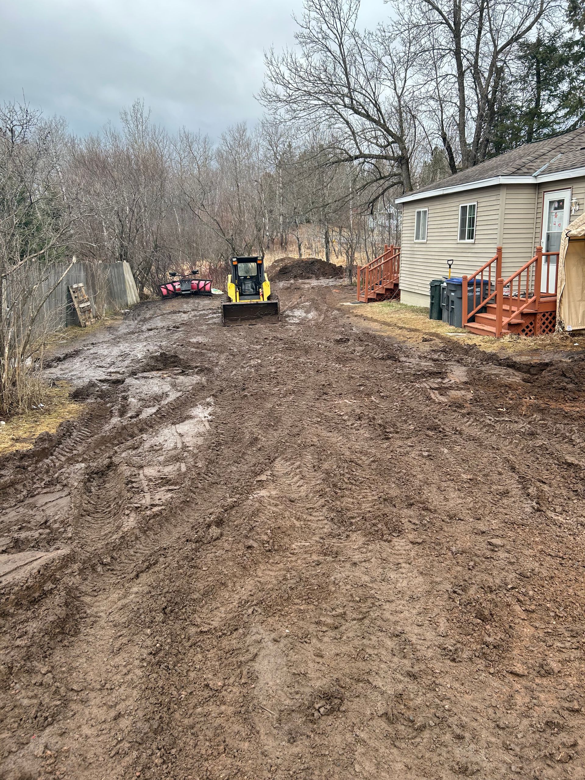 A muddy road leading to a house with a bulldozer in the background.