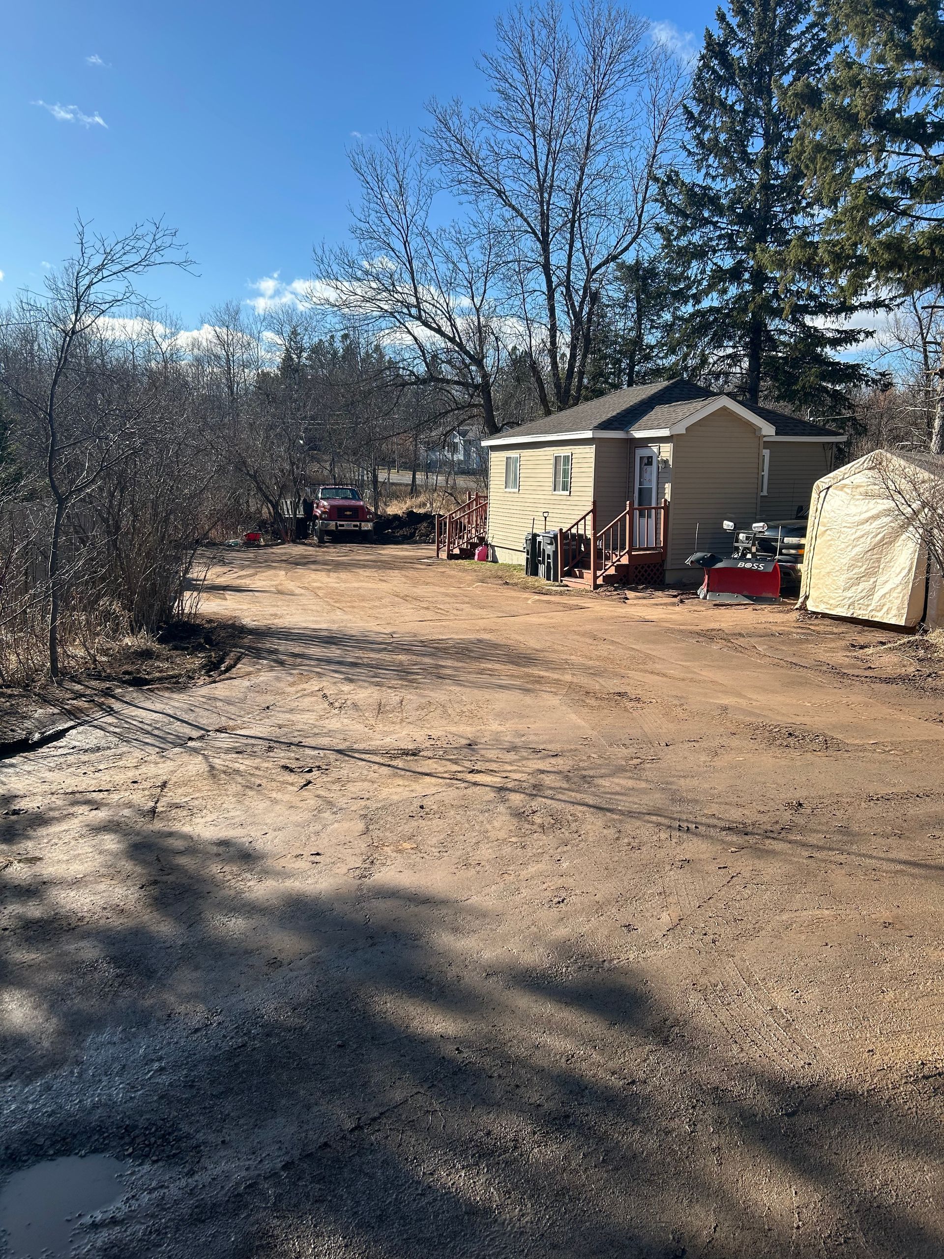 A house is sitting in the middle of a dirt field surrounded by trees.