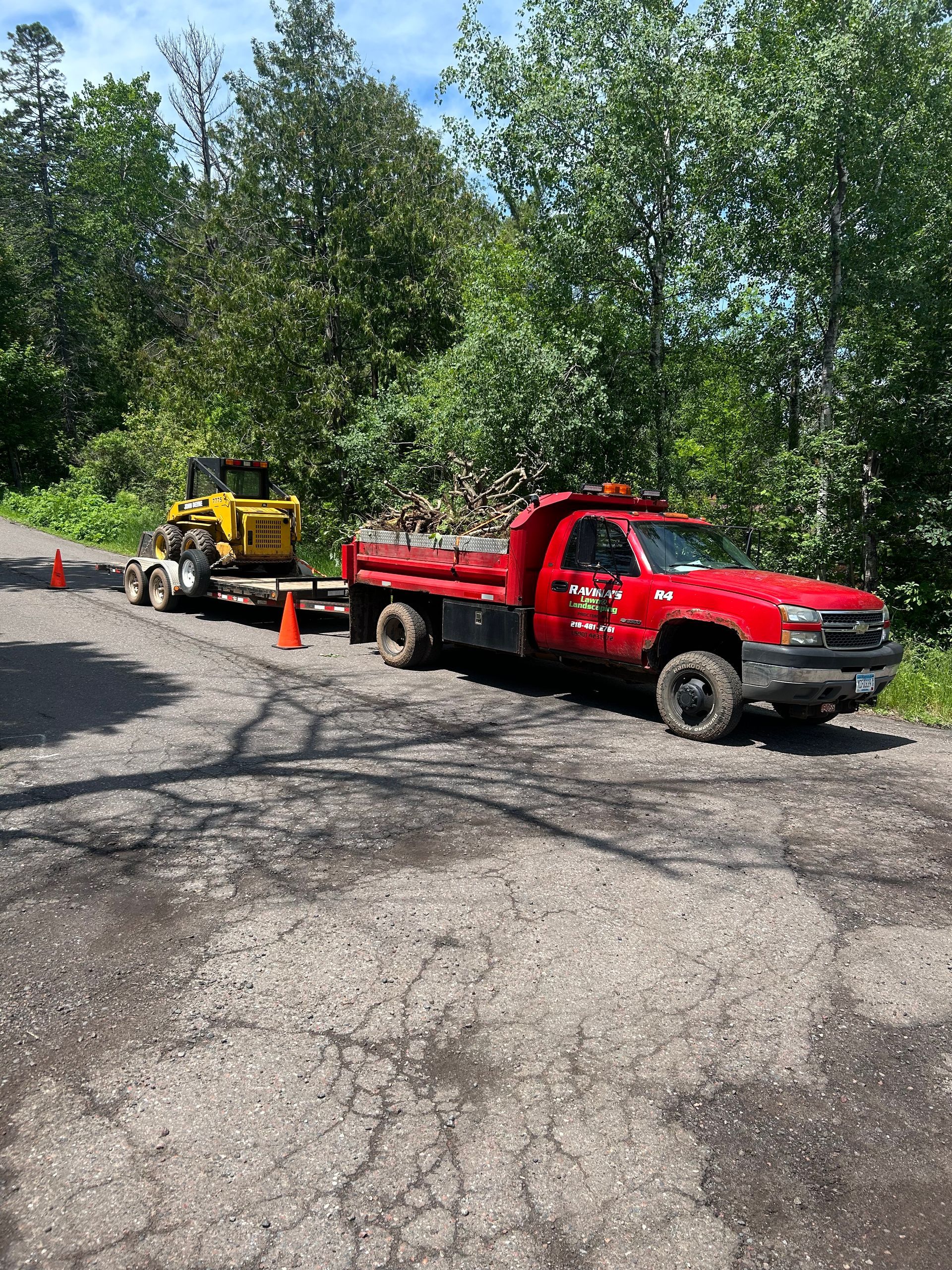 A red truck is towing a yellow tractor down a road.