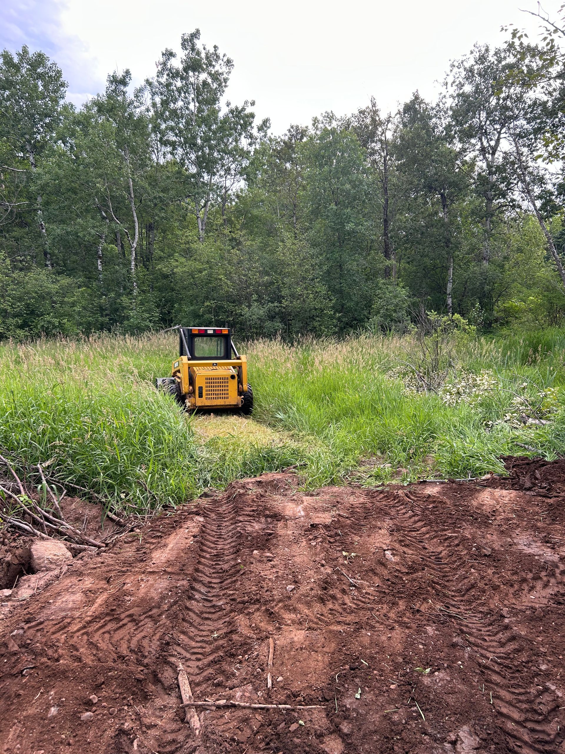 A yellow bulldozer is driving through a grassy field.