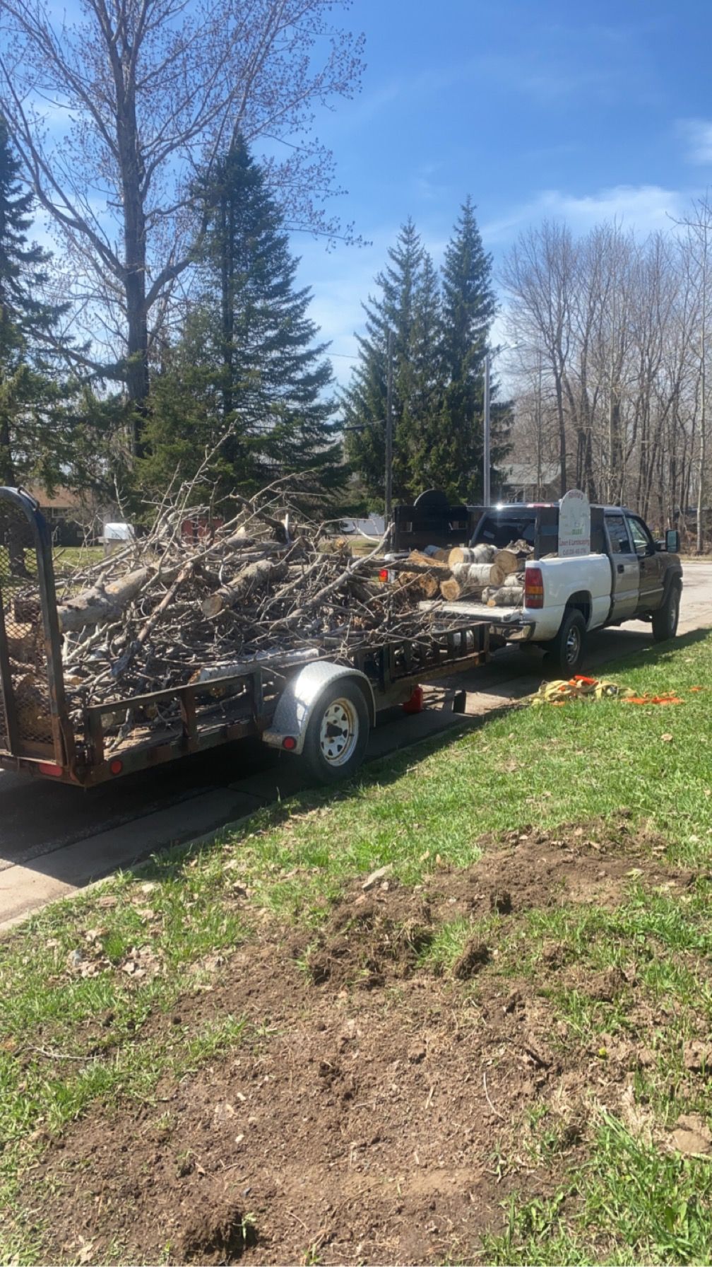 A white truck is towing a trailer full of logs.