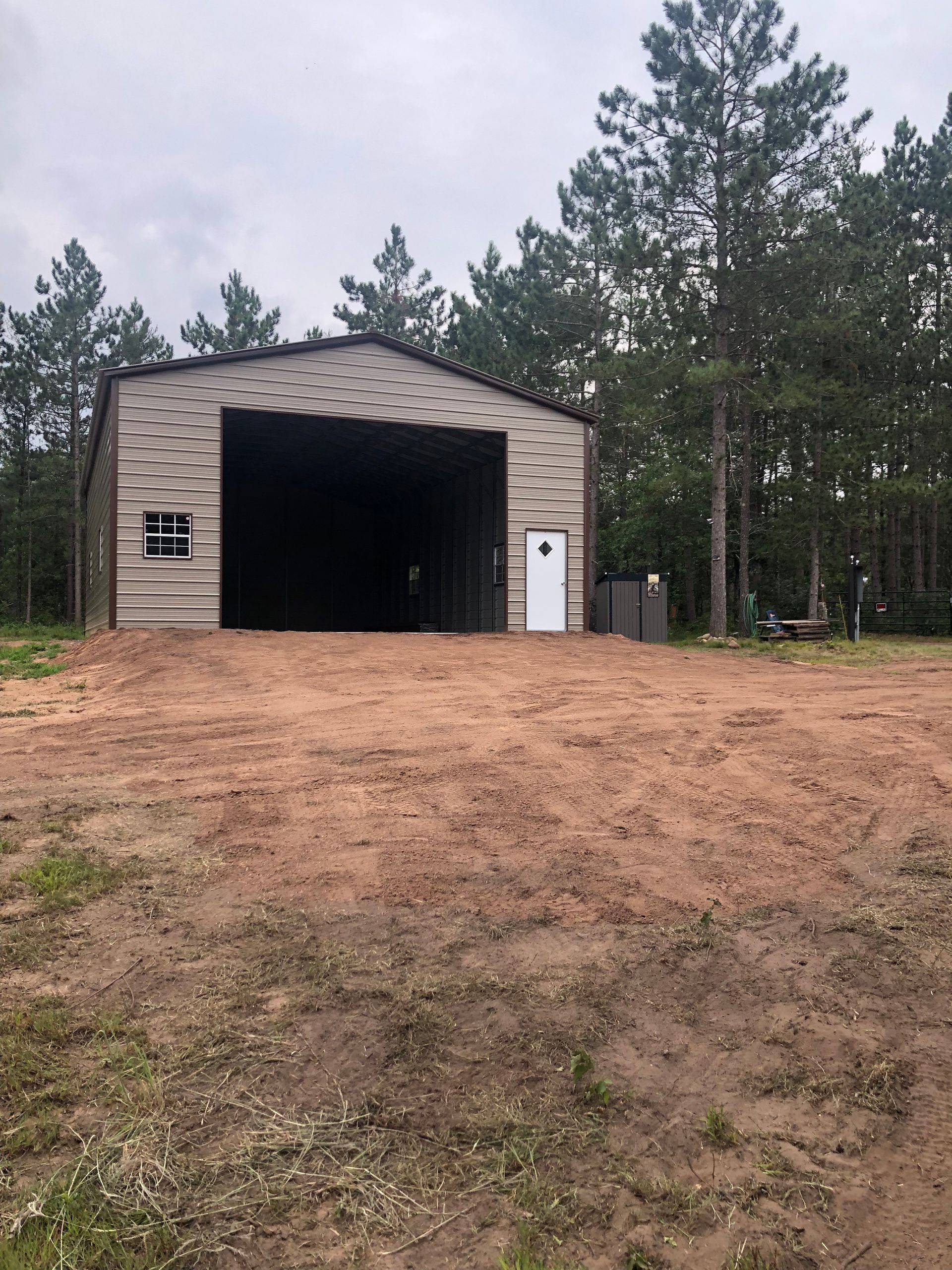 A large barn is sitting in the middle of a dirt field surrounded by trees.
