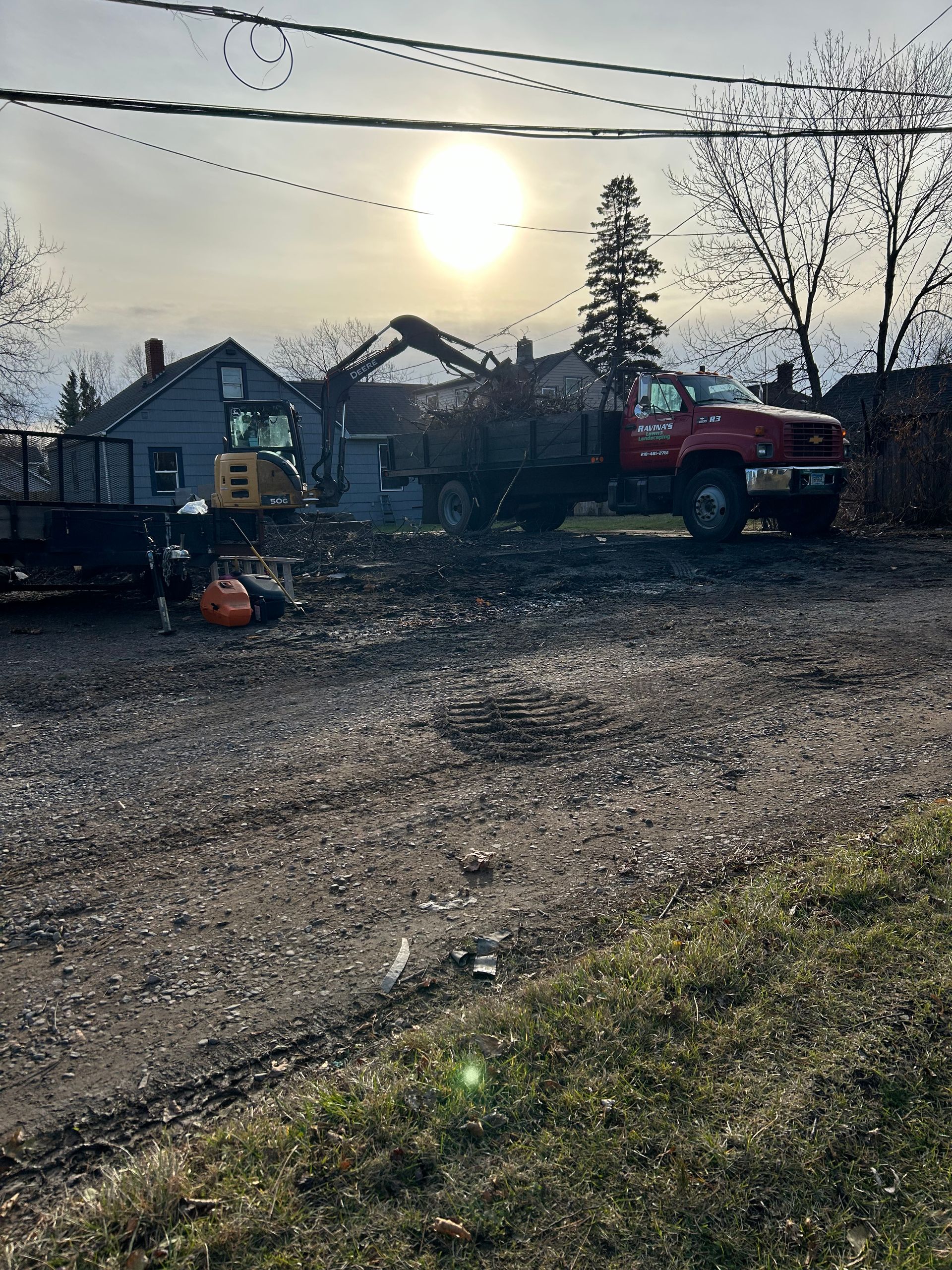 A red truck is parked in a gravel lot in front of a house being demolished.