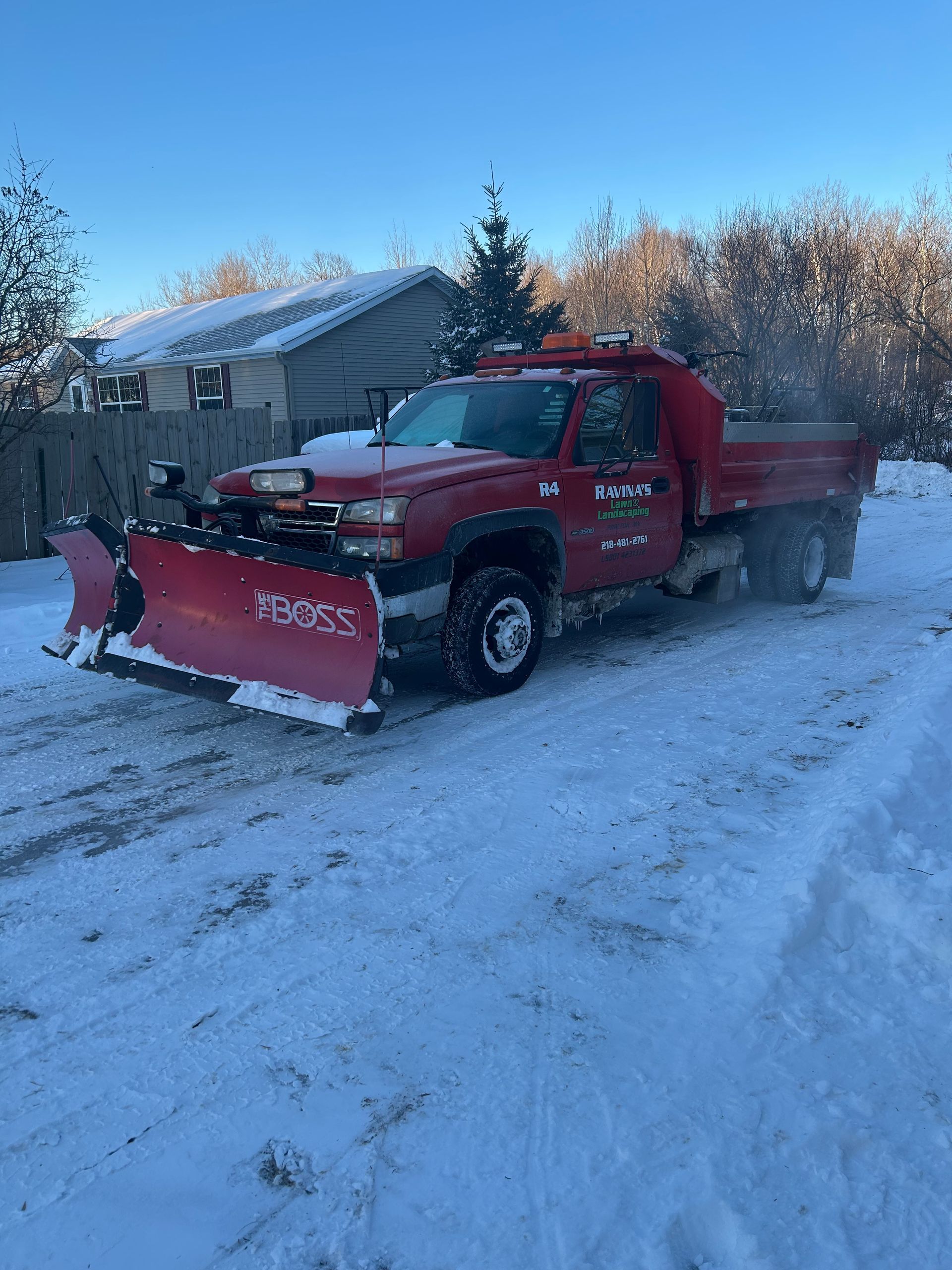A red truck with a snow plow on it is parked in the snow.