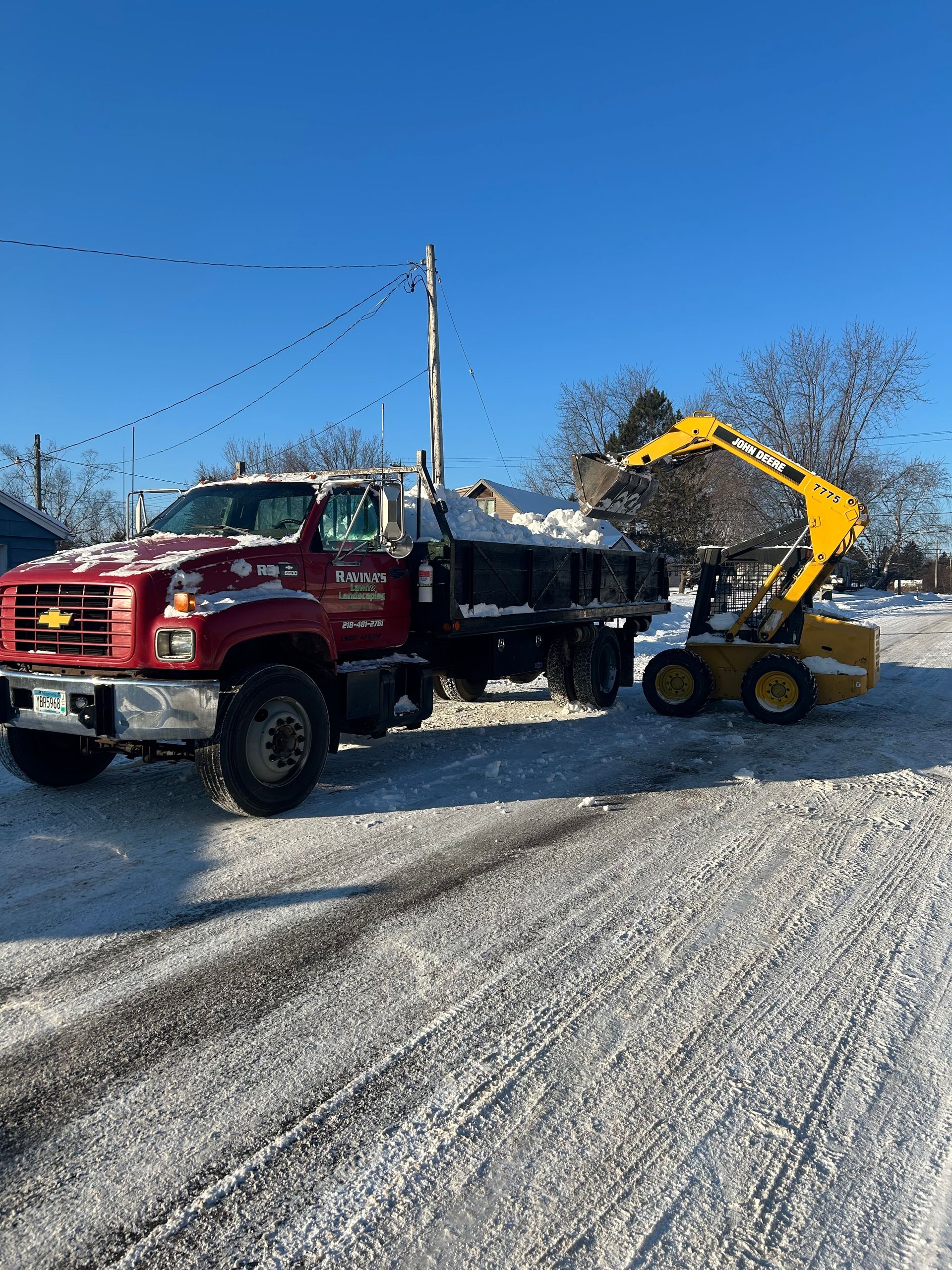 A red dump truck is driving down a snowy road next to a yellow snow plow.