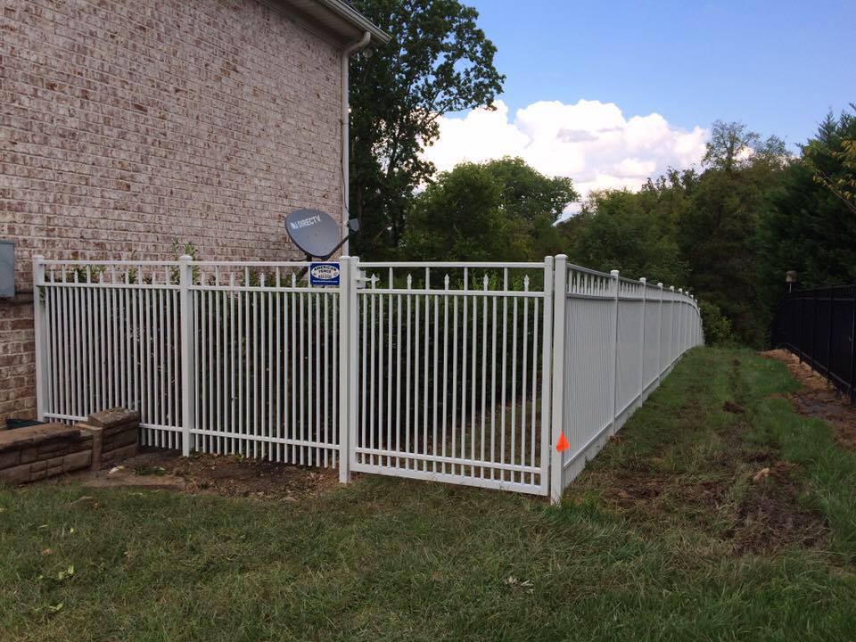 a white fence is surrounding a yard next to a house .