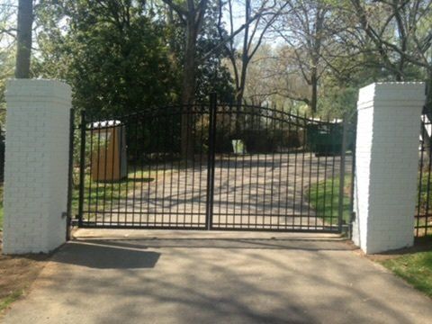 a wrought iron gate is open to a driveway surrounded by trees