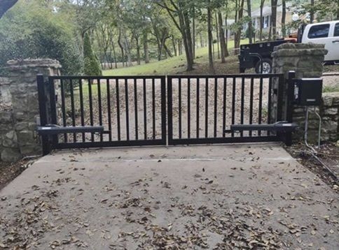 a black gate is open to a driveway with leaves on the ground .