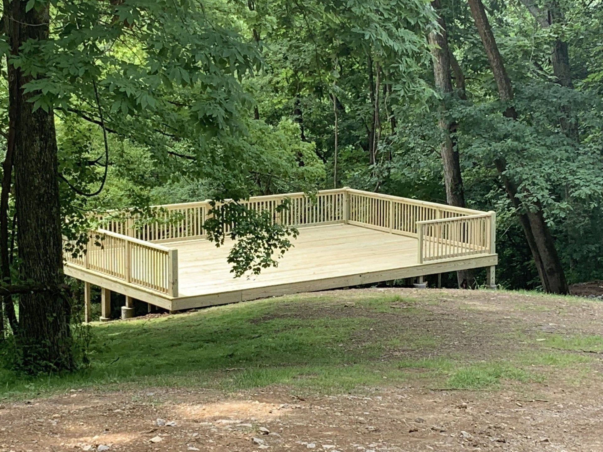 a wooden deck is sitting on top of a grassy hill in the middle of a forest .