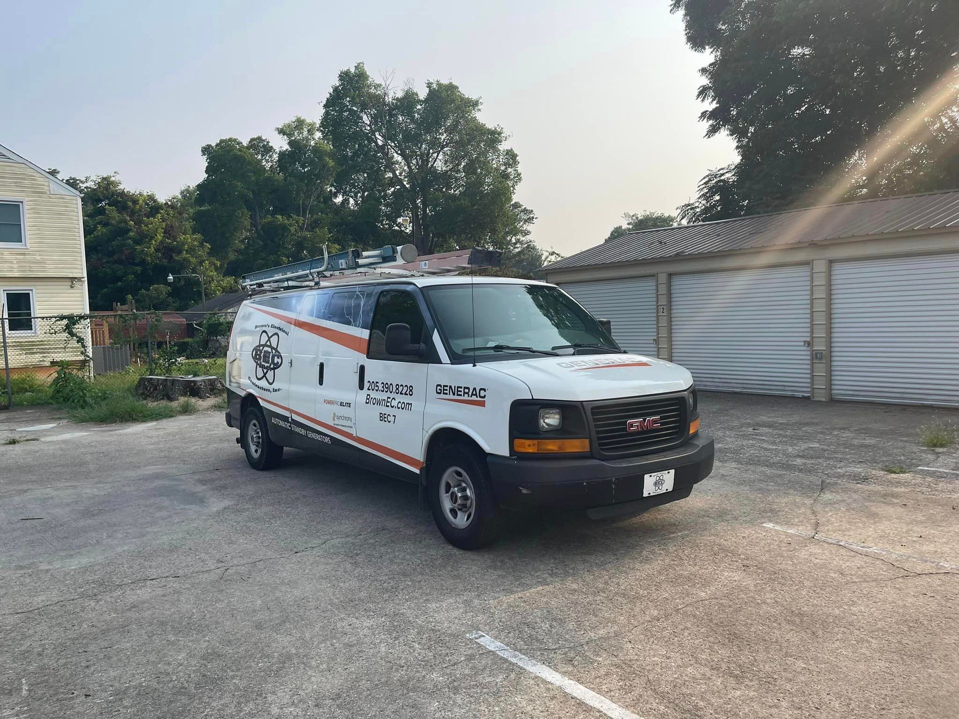 A white van is parked in a parking lot in front of a garage.