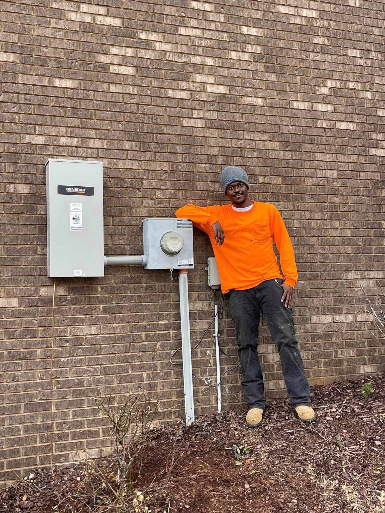 A man in an orange shirt is standing next to a brick wall.