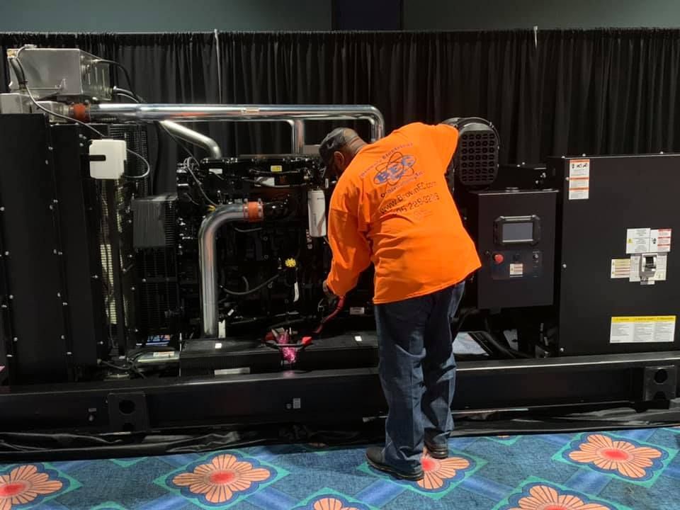 A man in an orange shirt is working on a generator.